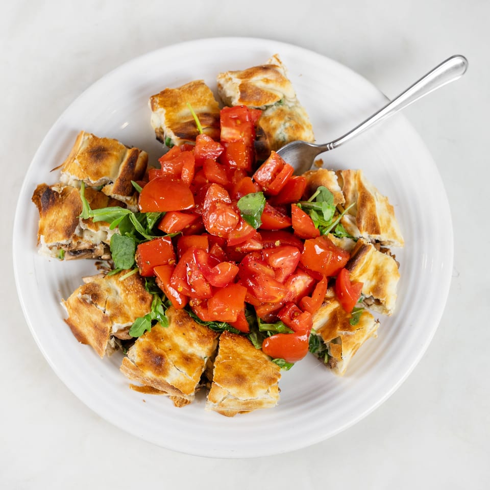 White plate of toasted pastry pieces topped with chopped tomatoes and fresh greens, with a fork resting alongside.