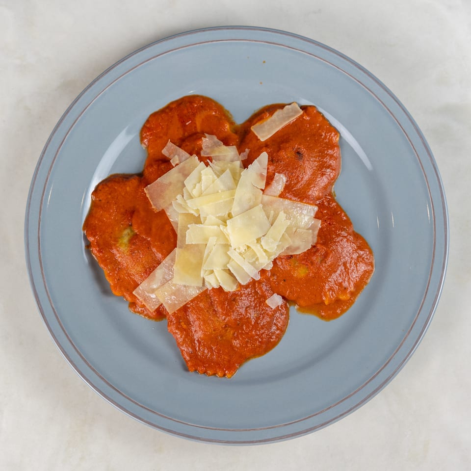 Ravioli topped with bright tomato sauce and shaved Parmesan cheese on a blue-rimmed plate.