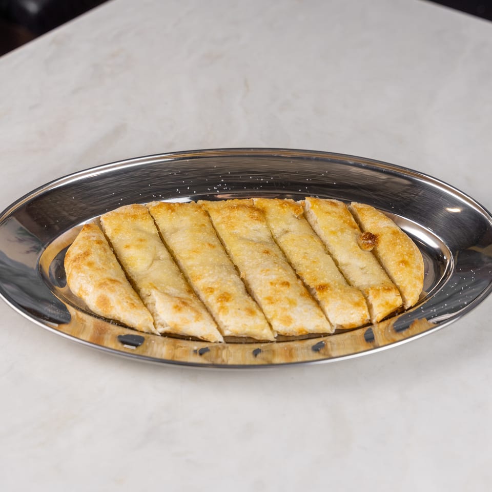 Golden-brown baked pastry strips arranged on a reflective oval serving platter atop a marble table.