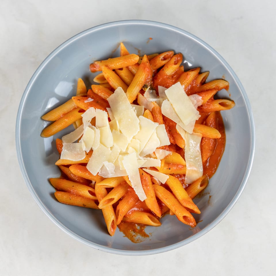 Overhead view of penne pasta in tomato sauce topped with shaved Parmesan cheese in a blue bowl.