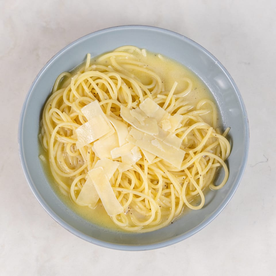 Overhead view of spaghetti in a light buttery sauce, topped with shaved Parmesan cheese in a blue bowl.