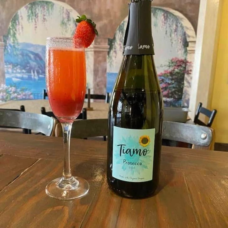 Tiamo Prosecco bottle beside a strawberry-garnished pink cocktail on a wooden restaurant table.