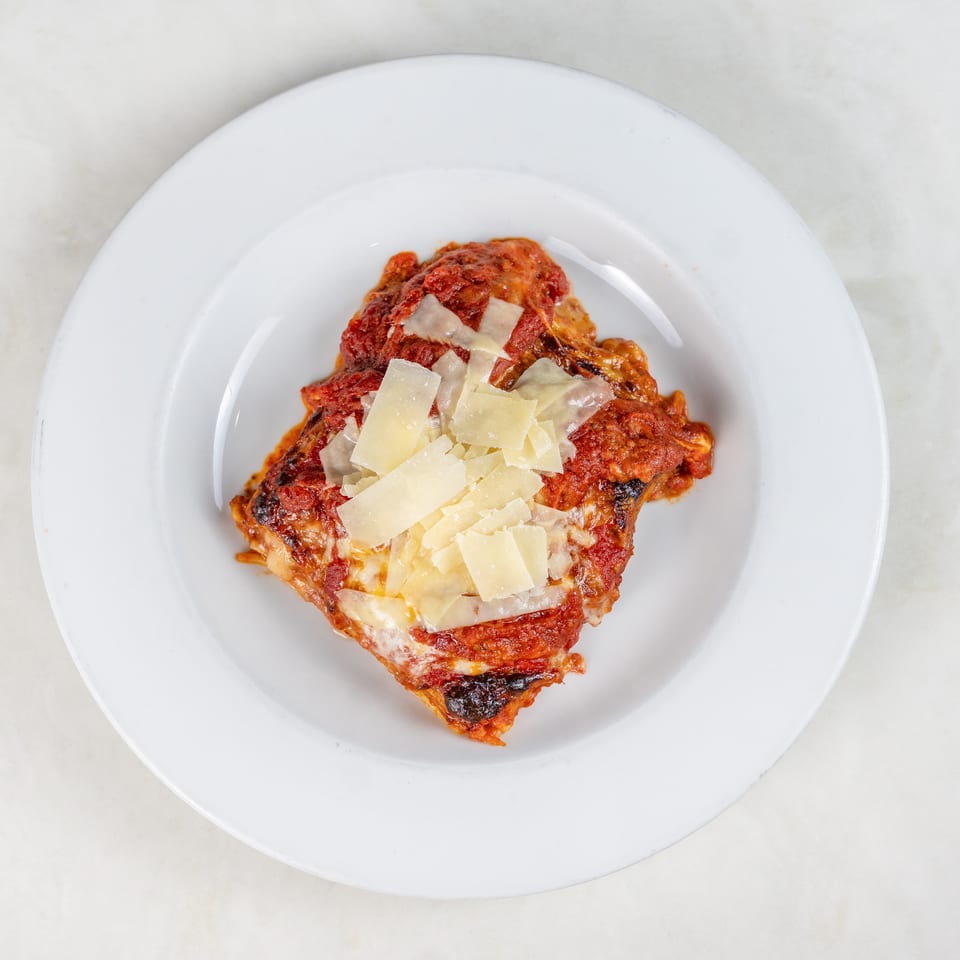Baked lasagna topped with melted cheese and Parmesan shavings, served on a white plate.