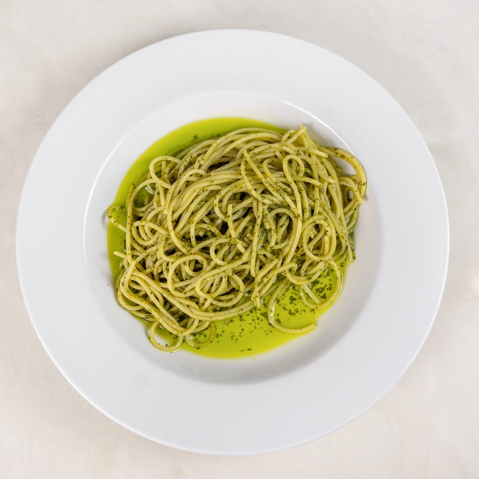 Spaghetti coated in green herb pesto and olive oil, served on a white plate.